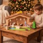 Preview: Kind spielt mit einer großen Weihnachtskrippe aus Naturholz mit Dachschindeln und Holzfiguren vor einem geschmückten Weihnachtsbaum.