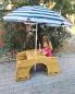 Mobile Preview: Ein Mädchen sitzt draußen unter einem Sonnenschirm auf der Bank der Outdoor-Sitzgarnitur.