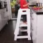 Preview: Kleinkind steht auf einem weißen, stabilen Lernturm an der Küchenzeile und schaut der Mutter beim kochen zu.