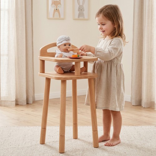 Kind füttert seine Puppe im Puppenhochstuhl aus Holz und erlebt ein fürsorgliches Rollenspiel