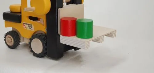 Detailaufnahme vom Kinder-Gabelstapler aus Holz mit Ladung einer Palette mit zwei Tonnen in grün und rot.
