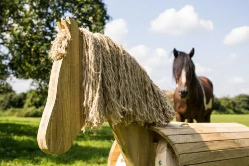 Holzpferd auf einer Wiese stehend, mit Pferd im Hintergrund.