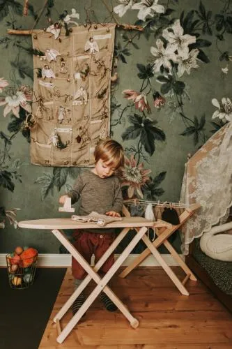 Kind bügelt am Holzbügelbrett Puppenwäsche, vor einem Wäscheständer