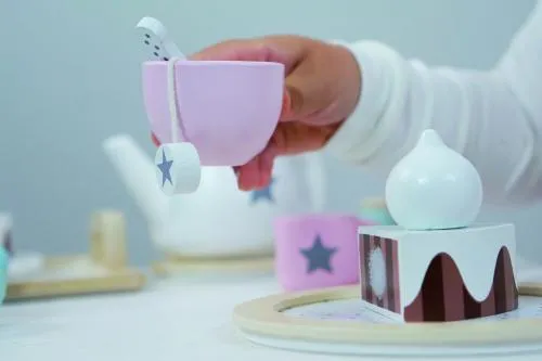 Eine Teetasse wird von einer Kinderhand gehalten, mit Kuchen im Hintergrund.