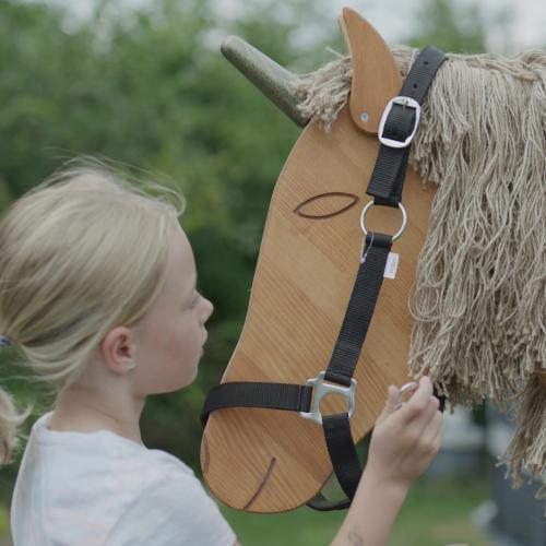 Kind legt dem Holzpferd Einhorn ein Halfter um