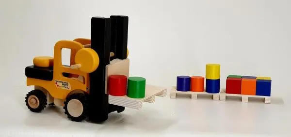 Kinder-Gabelstapler aus Holz mit gelber Baustellenbemalung, gummierten Reifen und als Ladung eine Palette mit zwei Tonnen in grün und rot. Weitere Paletten und bunte Klötze als Ladung im Hintergrund. Kinder-Gabelstapler aus Holz mit gelber Baustellenbemalung, gummierten Reifen und als Ladung eine Palette mit zwei Tonnen in grün und rot. Weitere Paletten und bunte Klötze als Ladung im Hintergrund.
