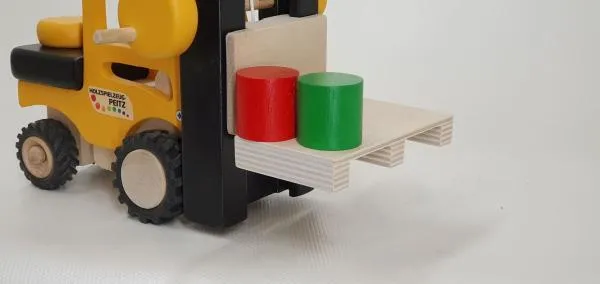 Detailaufnahme vom Kinder-Gabelstapler aus Holz mit Ladung einer Palette mit zwei Tonnen in grün und rot. Detailaufnahme vom Kinder-Gabelstapler aus Holz mit Ladung einer Palette mit zwei Tonnen in grün und rot.