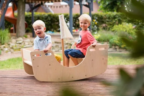 Zwei Kinder sitzen in Holz-Wippe draußen im Garten. Zwei Kinder sitzen in Holz-Wippe draußen im Garten.