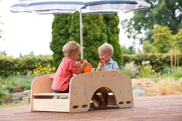 Zwei Kinder tauschen sich unter einem Sonnenschirm auf der Garten-Sitzgarnitur aus. Zwei Kinder tauschen sich unter einem Sonnenschirm auf der Garten-Sitzgarnitur aus.
