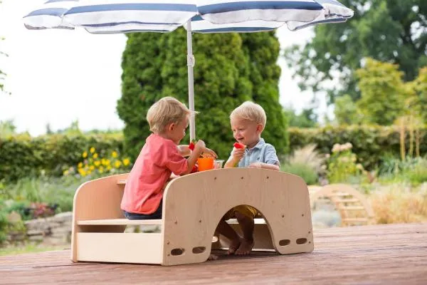 Zwei Kinder tauschen sich unter einem Sonnenschirm auf der Garten-Sitzgarnitur aus. Zwei Kinder tauschen sich unter einem Sonnenschirm auf der Garten-Sitzgarnitur aus.