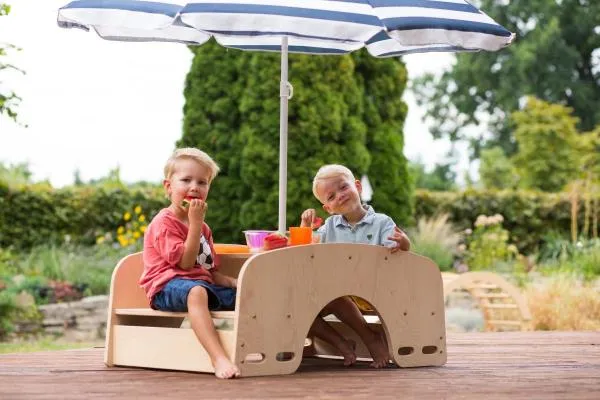 Zwei Kinder picknicken an der Garten-Sitzgarnitur unter einem Sonnenschirm. Zwei Kinder picknicken an der Garten-Sitzgarnitur unter einem Sonnenschirm.
