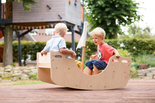 Zwei Kinder nutzen die Holz-Wippe draußen im Garten. Zwei Kinder nutzen die Holz-Wippe draußen im Garten.