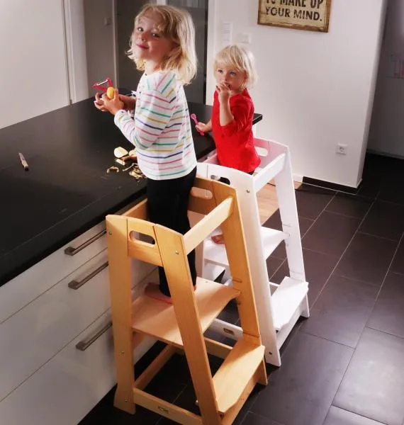 Kinder stehen auf Lerntürmen an der Küchenzeilen und essen. Diese sind höhenverstellbar und aus Massivholz. Kinder stehen auf Lerntürmen an der Küchenzeilen und essen. Diese sind höhenverstellbar und aus Massivholz.