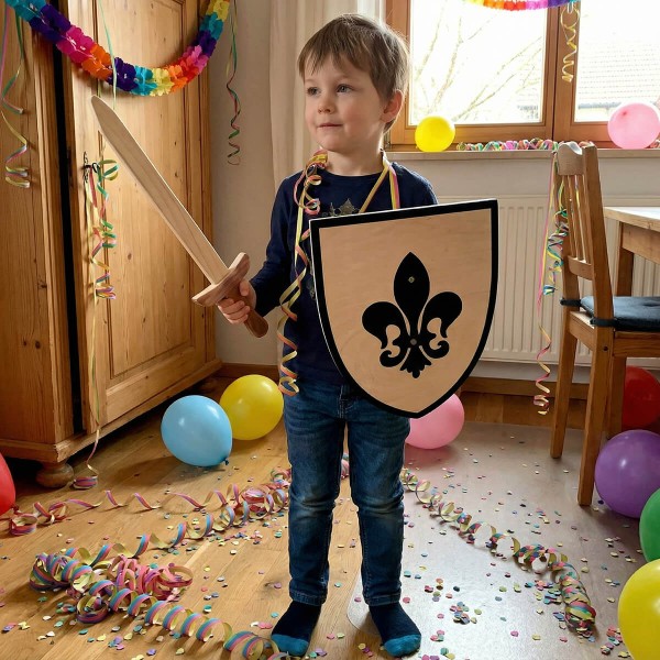 Kind hält Holzschild mit Lilienmotiv und Holzschwert beim fantasievollen Spiel