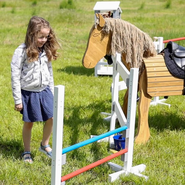Kind springt mit Hobbyhorse über die Kinder Springhürde aus Holz im Garten