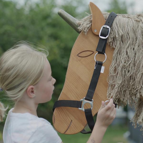 Kind legt dem Holzpferd Einhorn ein Halfter um Kind legt dem Holzpferd Einhorn ein Halfter um