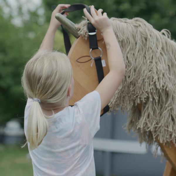 Kind spielt mit dem Holzpferd Einhorn und legt ihm ein Halfter an. Kind spielt mit dem Holzpferd Einhorn und legt ihm ein Halfter an.